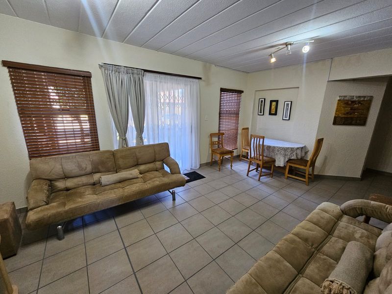 A spacious living and dining area featuring neutral tiled flooring, slatted window blinds, and a sliding glass door providing access to the exterior.