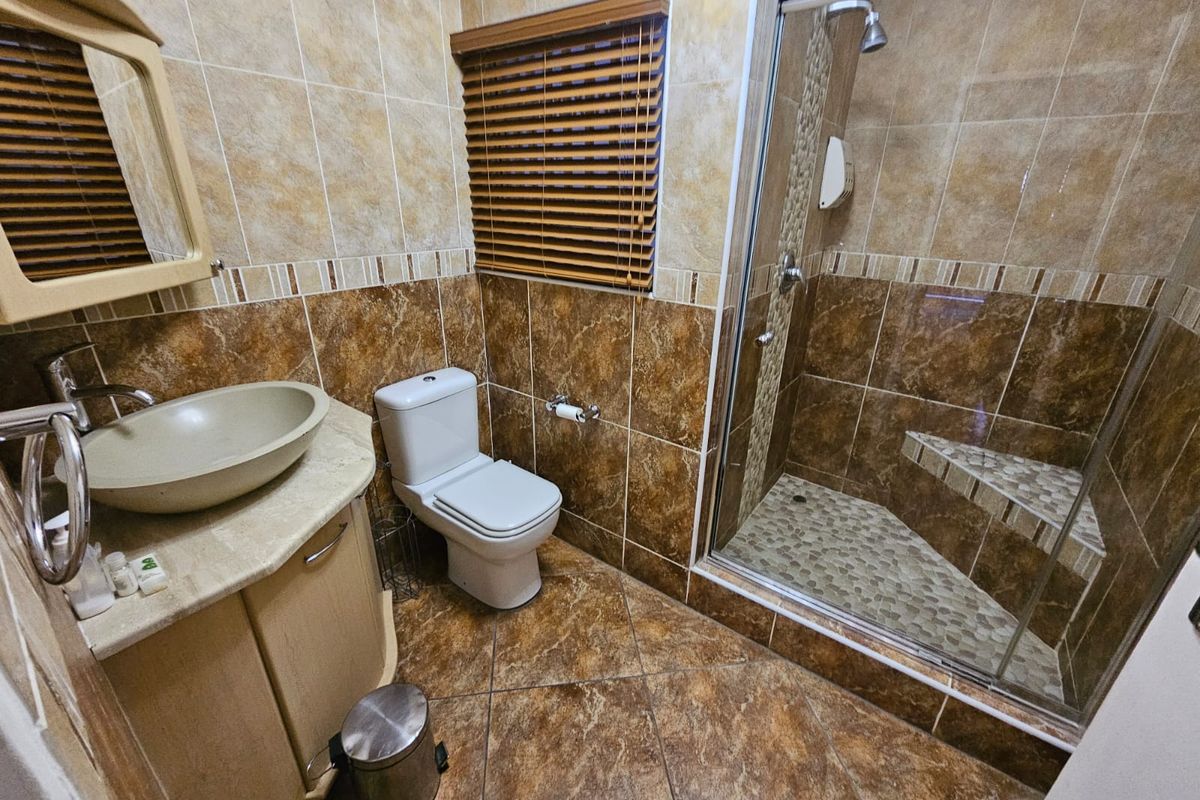 A well-maintained bathroom featuring a vessel sink vanity, a toilet, and a walk-in shower with a built-in bench and decorative tiled finishes.