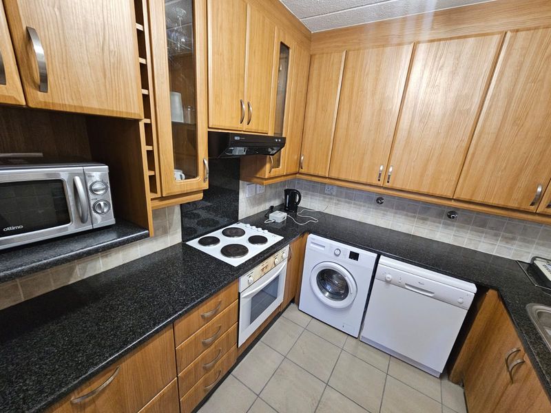 A functional kitchen featuring wood-finish cabinetry, dark granite countertops, tiled backsplash, and integrated appliances including an oven and hob.
