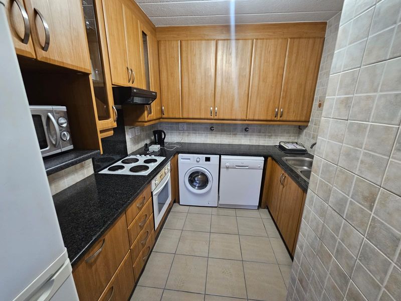 A functional kitchen featuring wooden cabinetry, granite countertops, an electric hob, built-in oven, and integrated space for laundry and dishwashing appliances.