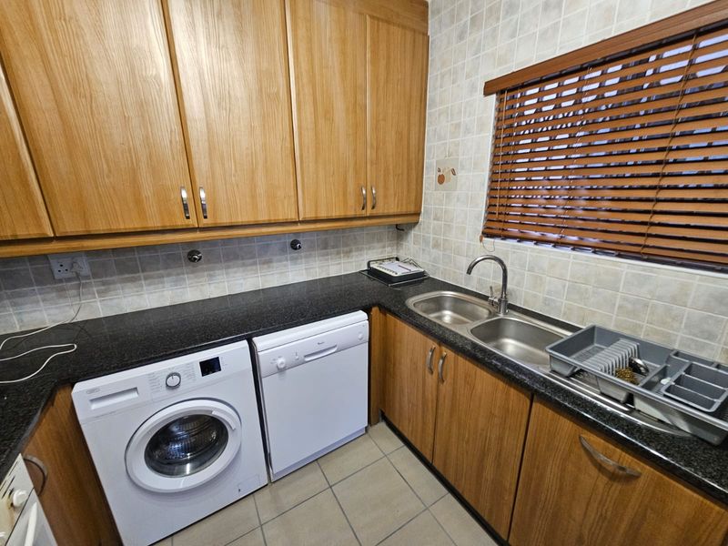 A functional scullery featuring laminate cabinetry, granite countertops, a double bowl stainless steel sink, and tiled finishes.