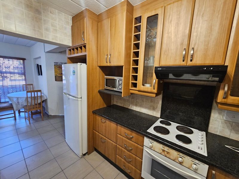 A functional kitchen featuring wooden cabinetry, granite countertops, and built-in electric cooking appliances, with tiled flooring and a tiled backsplash.