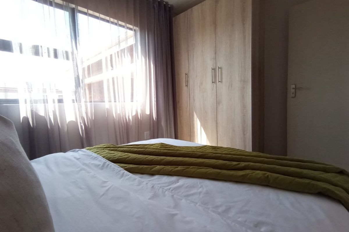 A well-lit bedroom featuring built-in wooden cabinetry and large windows with curtains, providing a clean and functional living space.