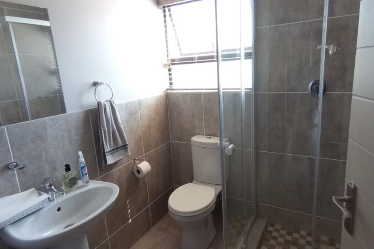 A modern bathroom featuring a pedestal basin, a tiled shower enclosure with a glass door, and a standard toilet.