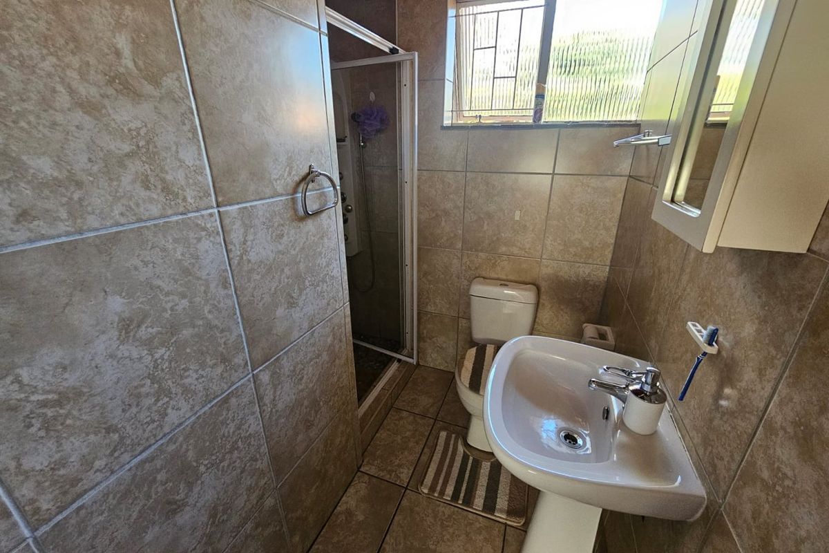 A functional bathroom featuring a pedestal basin, a toilet, and a glass-enclosed shower with neutral floor-to-ceiling tiling.