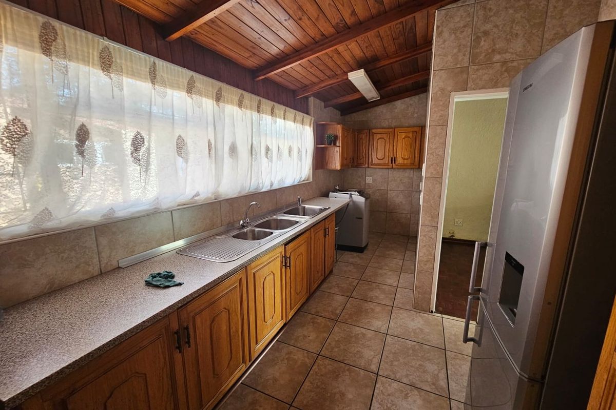 A functional kitchen featuring wooden cabinetry, tiled flooring, a double-basin sink, and a timber-paneled ceiling, providing a practical workspace.