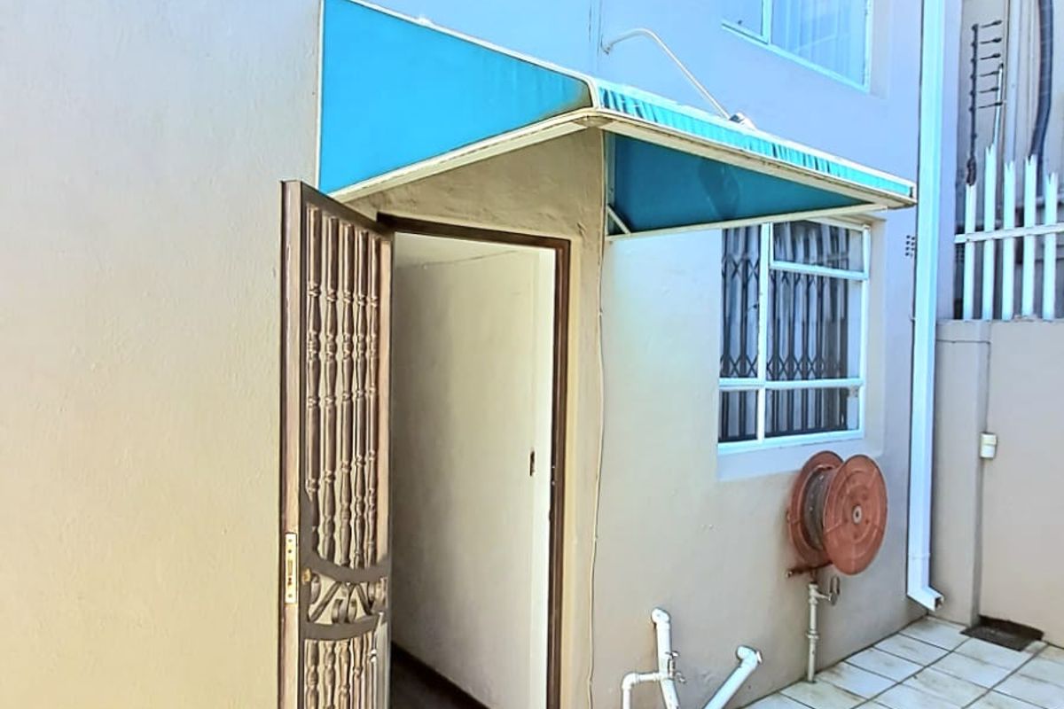 Rear exterior view of the townhouse featuring a tiled patio area, security gate, and a fixed awning over the entrance.