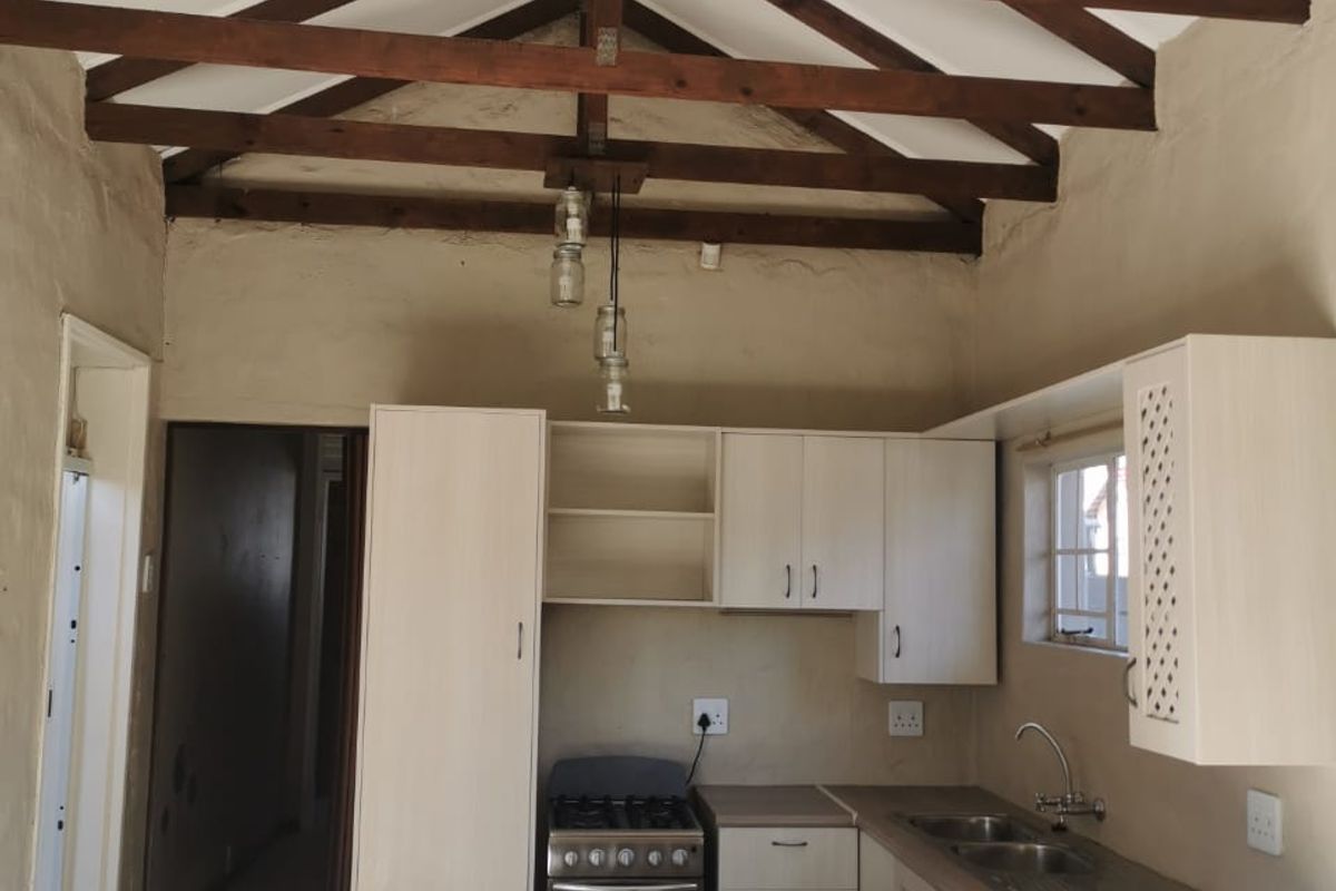 Kitchen featuring exposed timber roof trusses, built-in cabinetry, stainless steel sink, and a gas stove, with tiled flooring throughout.