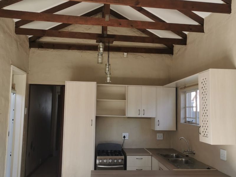 Kitchen featuring exposed timber roof trusses, built-in cabinetry, stainless steel sink, and a gas stove, with tiled flooring throughout.