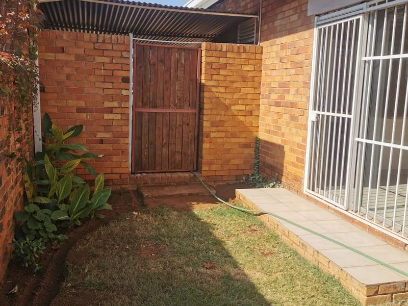 A private rear courtyard featuring a brick wall, a wooden security gate, a small tiled patio area, and a lawn.