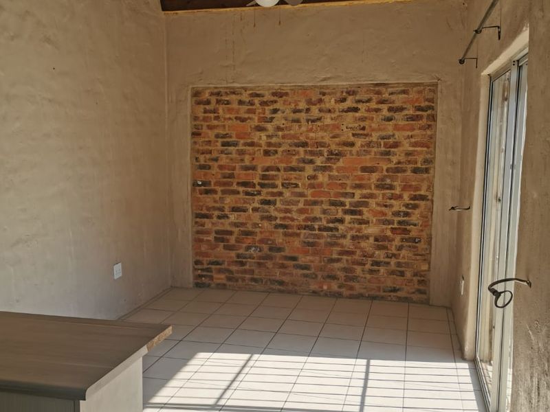 An empty living area featuring exposed timber roof trusses, a brick feature wall, tiled floors, and a sliding glass door leading outdoors.