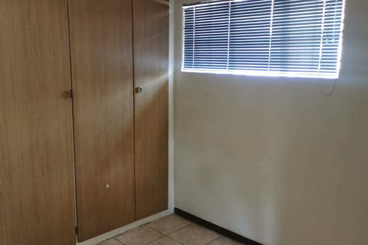 An empty bedroom featuring tiled flooring, built-in wooden cupboards, and a window fitted with venetian blinds.