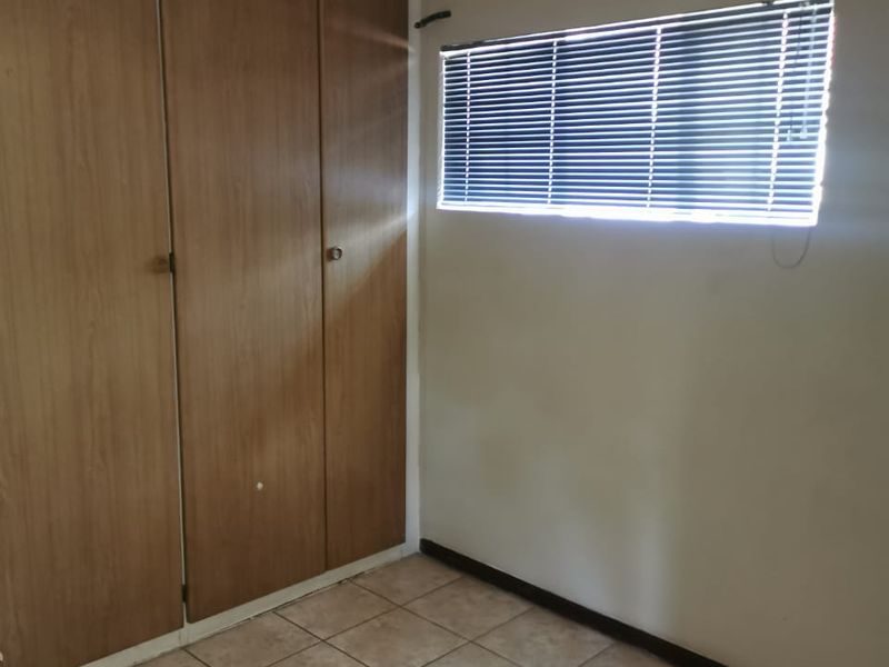 An empty bedroom featuring tiled flooring, built-in wooden cupboards, and a window fitted with venetian blinds.