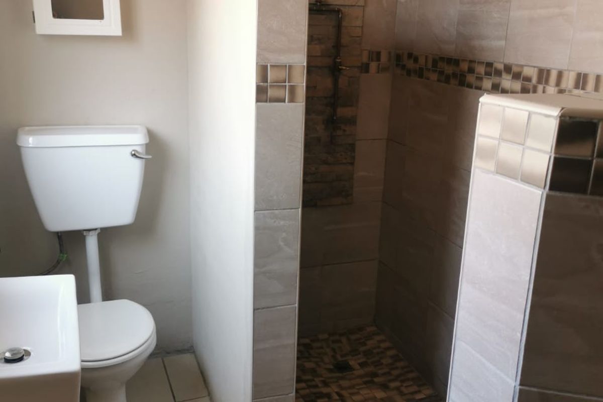 A modern bathroom featuring a walk-in shower with exposed copper plumbing, a stone feature wall, tiled flooring, and a wall-mounted basin.