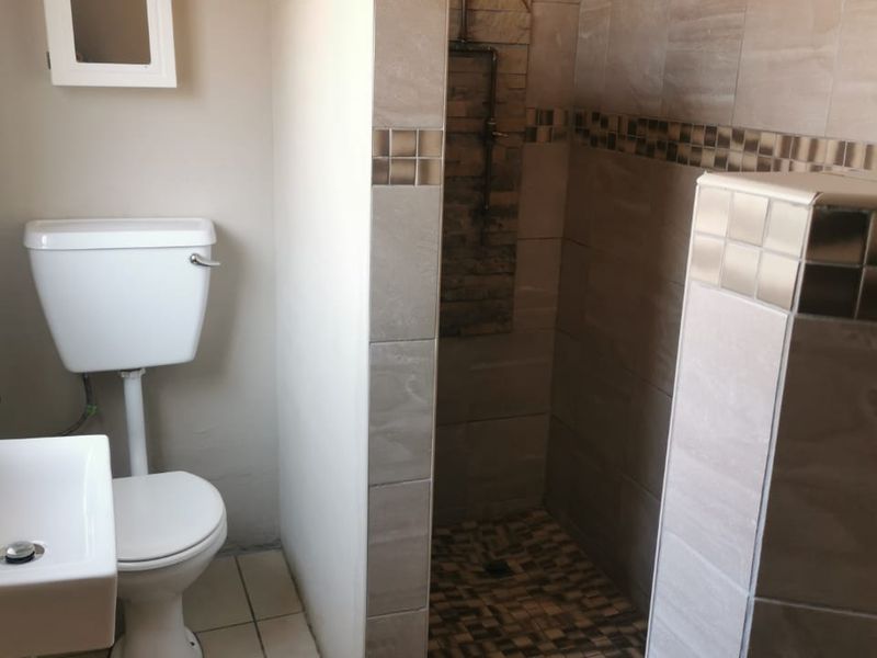 A modern bathroom featuring a walk-in shower with exposed copper plumbing, a stone feature wall, tiled flooring, and a wall-mounted basin.