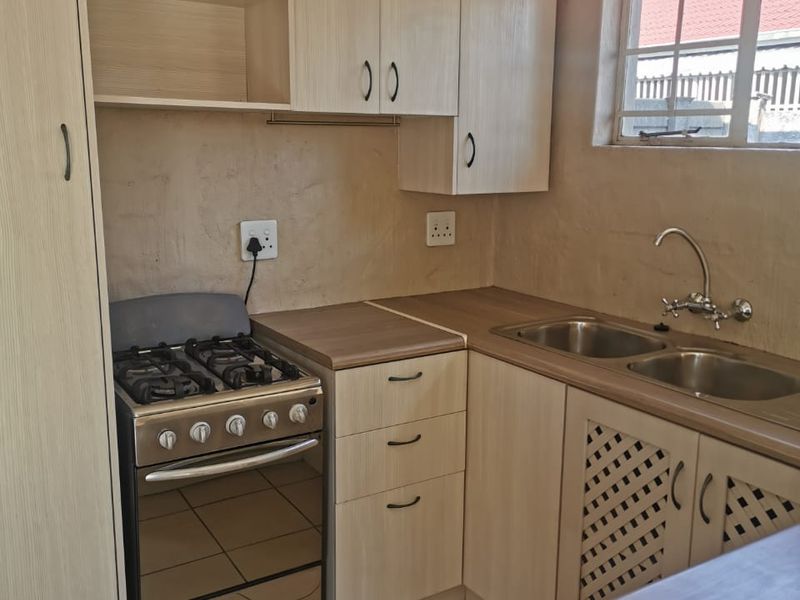 A functional kitchen featuring light wood-finish cabinetry, laminate countertops, a double stainless steel sink, and a gas stove with tiled flooring.