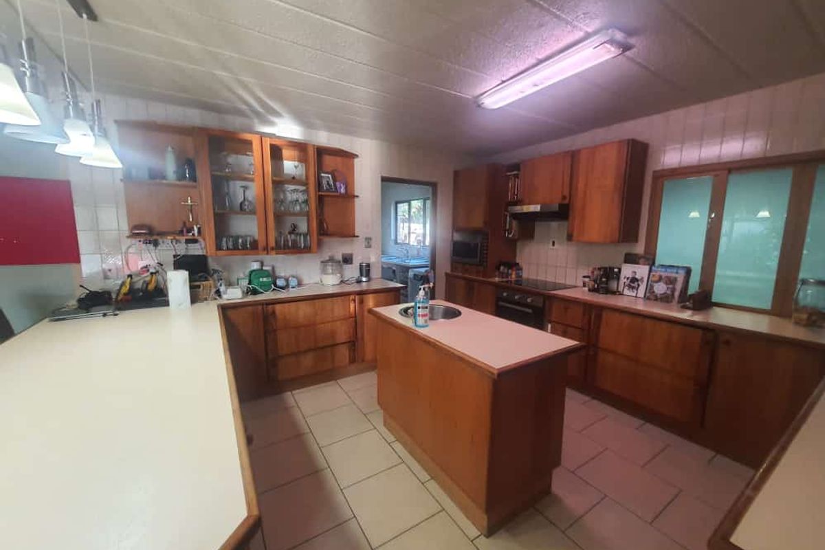 A spacious kitchen featuring extensive wooden cabinetry, a central island with a sink, and tiled flooring, offering a functional layout with ample storage.
