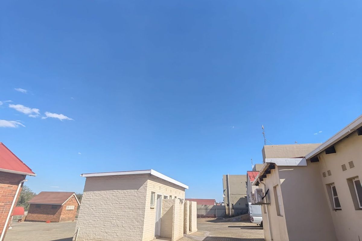 Exterior view of the property grounds featuring paved courtyard areas and detached utility structures under a clear blue sky.