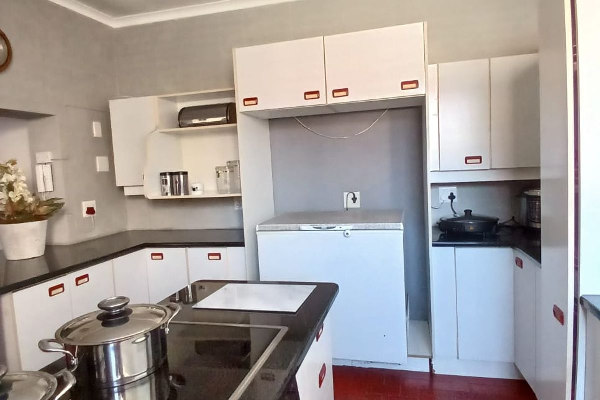 A functional kitchen featuring white cabinetry, dark countertops, a central island with a built-in hob, and red tiled flooring.