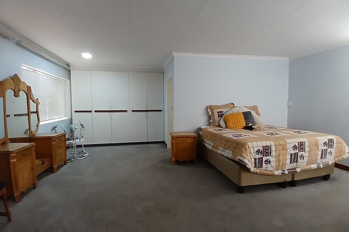 Spacious bedroom featuring neutral wall tones, fitted floor-to-ceiling built-in wardrobes, and carpeted flooring.