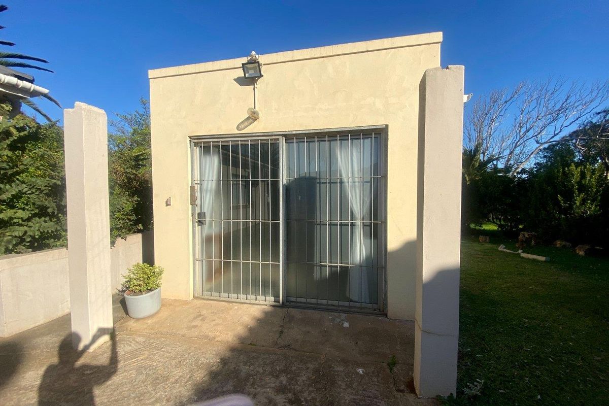Exterior view of a small office structure featuring a sliding glass door with security bars and an external wall-mounted light fixture.