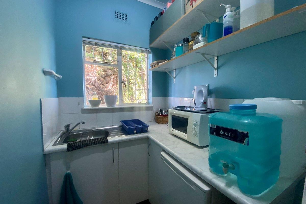 A compact kitchenette or utility area featuring a stainless steel sink, laminate countertops, and open wall-mounted shelving.