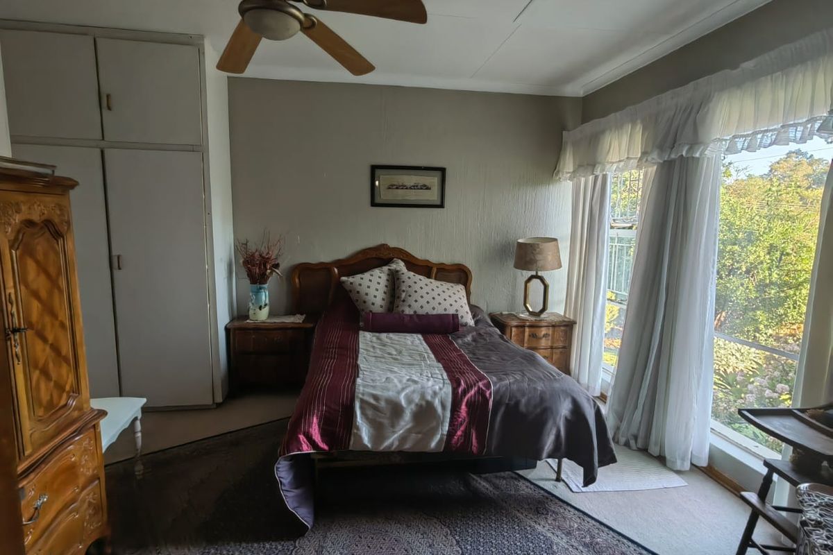 A bedroom featuring built-in cupboards, a ceiling fan, and large windows providing natural light and garden views.
