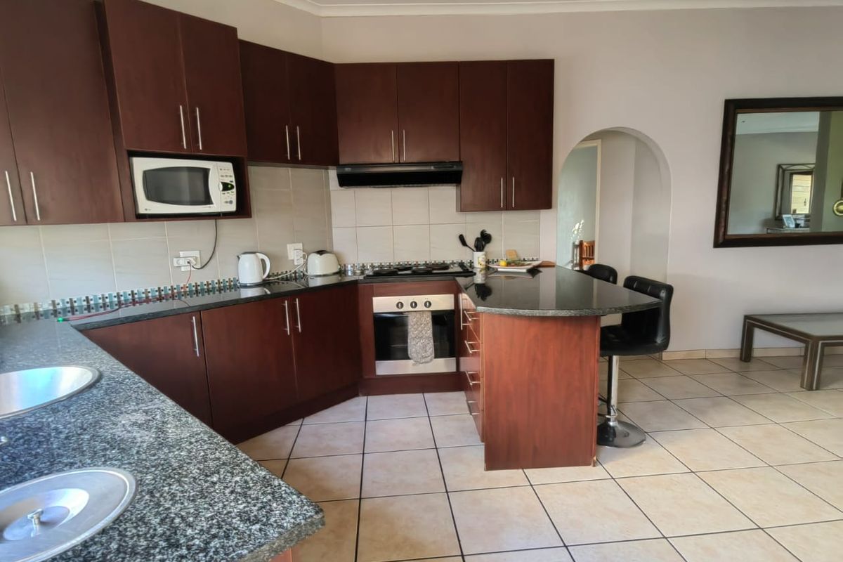 A functional kitchen featuring dark wood cabinetry, granite countertops, a built-in oven, hob, and extractor fan, with tiled flooring throughout.