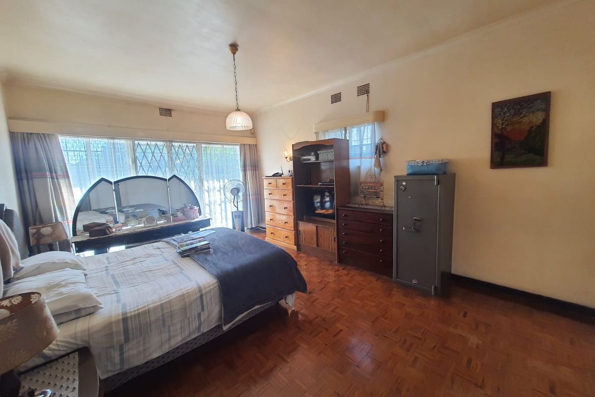 A spacious bedroom featuring classic parquet flooring, large windows with security bars, and a neutral color palette.