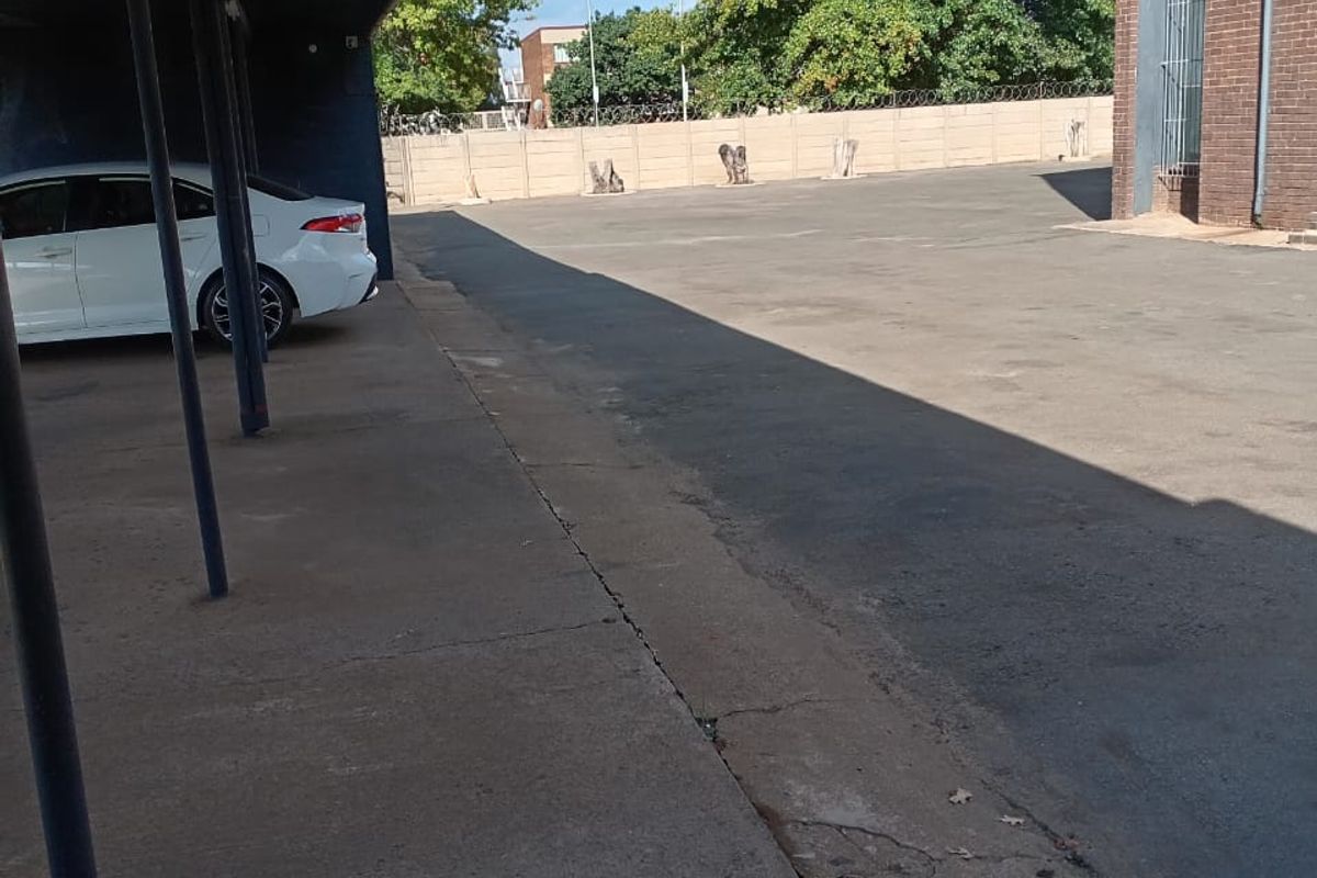 An outdoor parking area featuring a covered carport structure adjacent to a brick building facade.