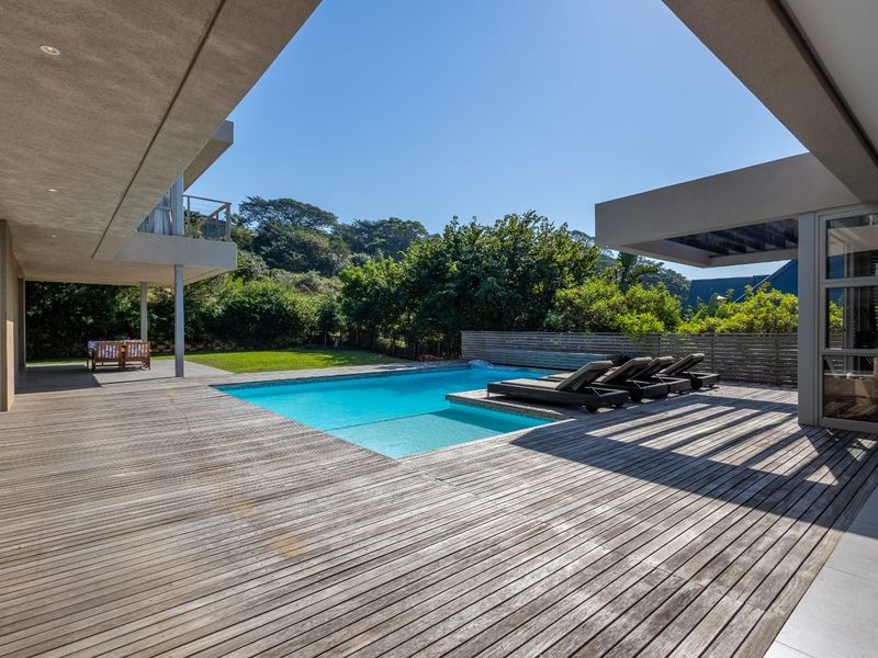 Spacious outdoor entertainment area featuring a large swimming pool, expansive timber decking, and a covered patio overlooking the private garden.