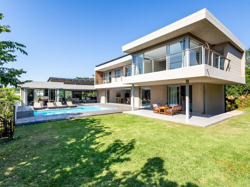 A modern two-story residence featuring a spacious lawn, a swimming pool with timber decking, and expansive balconies overlooking the garden.