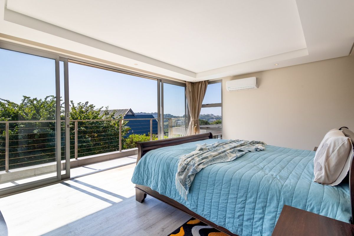 Spacious bedroom featuring large sliding glass doors that open onto a private balcony, complemented by a wall-mounted air conditioning unit and recessed ceiling lighting.
