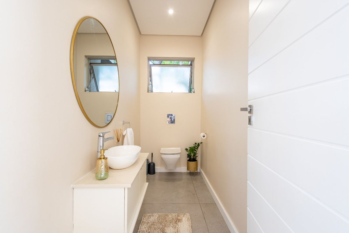 A modern guest bathroom featuring a wall-mounted toilet, a sleek vanity with a vessel sink, and neutral floor tiling.
