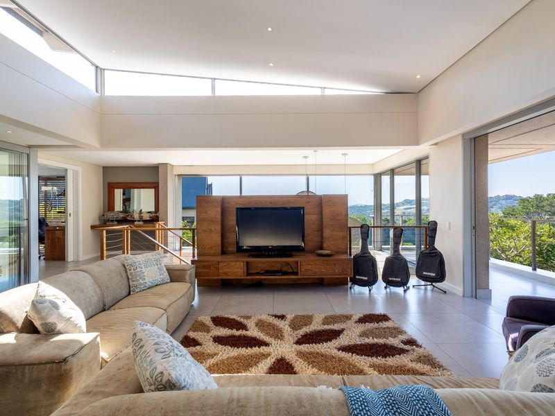 Spacious open-plan living area featuring high raked ceilings, clerestory windows, large format floor tiles, and seamless flow to an expansive outdoor balcony.