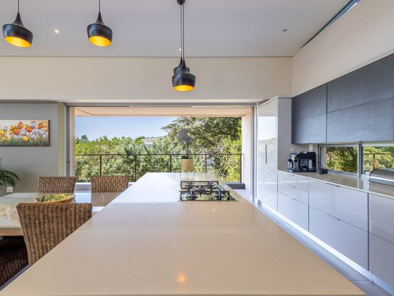 Modern open-plan kitchen featuring a large stone-topped island with integrated gas hob, sleek cabinetry, and seamless flow to an outdoor balcony.
