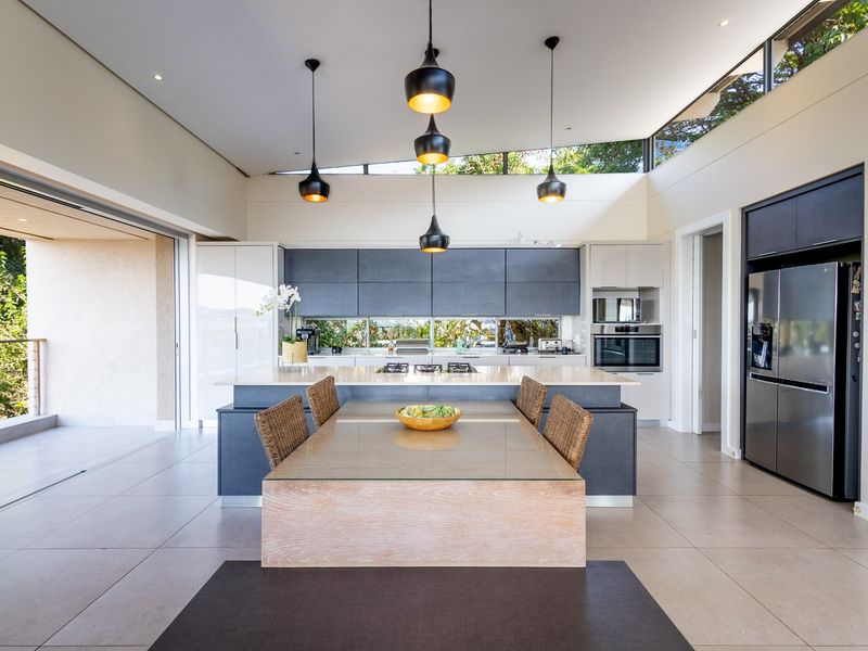 Modern open-plan kitchen featuring a central island with integrated cooktop, sleek cabinetry, built-in oven, and high-level clerestory windows providing natural light.