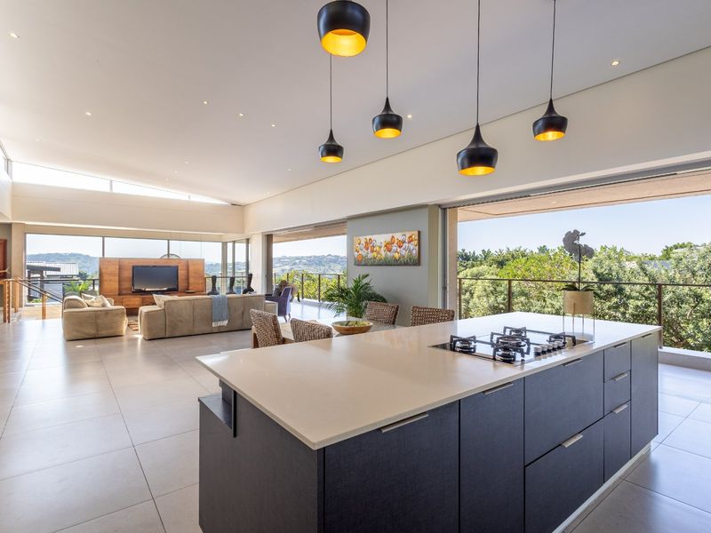 Spacious open-plan living area featuring a modern kitchen island with integrated gas hob, flowing seamlessly onto a covered balcony with scenic views.