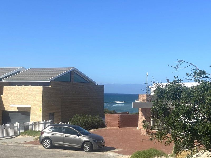 A view of the coastal residential property showing the exterior facade, paved driveway, and ocean horizon in the background.