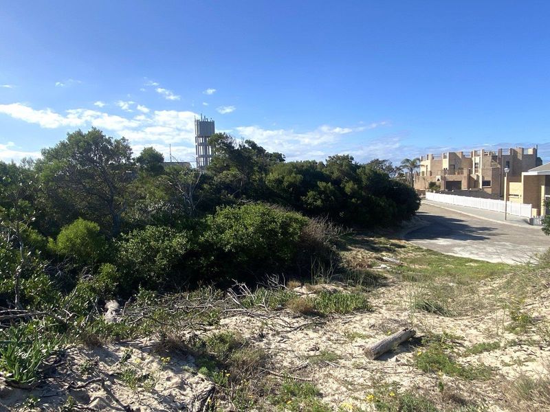 A view of the vacant residential land featuring natural coastal vegetation, sandy terrain, and proximity to established neighborhood infrastructure and paved road access.