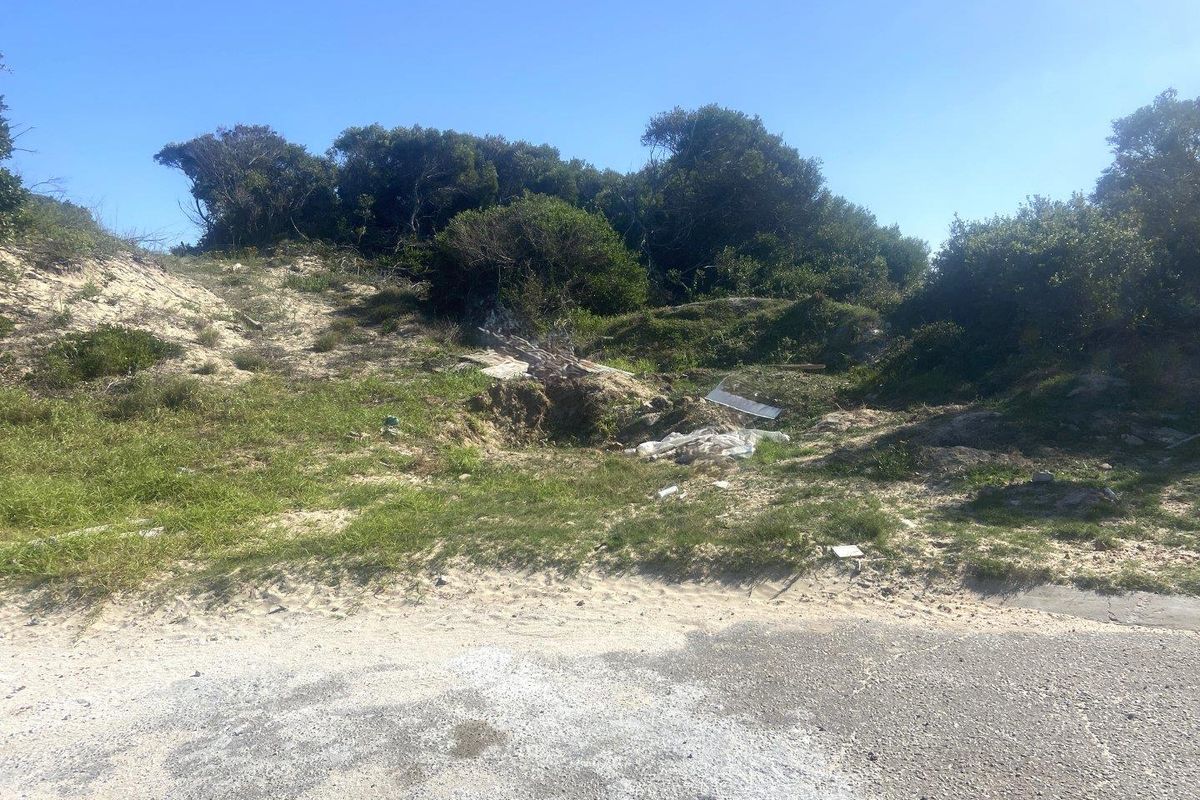 A vacant residential plot featuring natural coastal dune vegetation and direct street access, offering a blank canvas for future development.