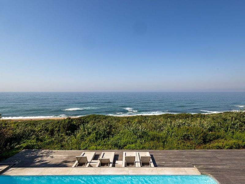 A stunning outdoor pool area featuring timber decking and an expansive, unobstructed view of the ocean and coastal landscape.