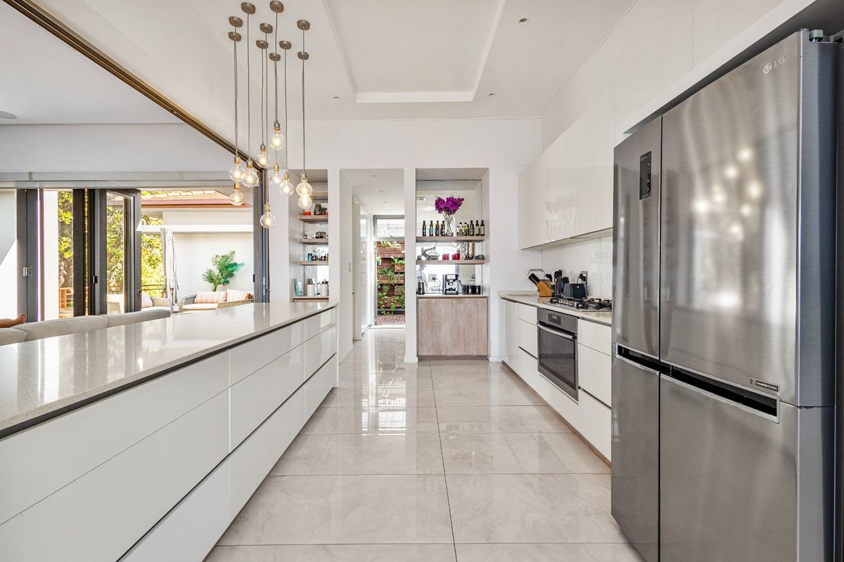 Modern kitchen featuring a large central island, high-gloss cabinetry, integrated appliances, and sleek porcelain flooring, flowing seamlessly into the outdoor living area.