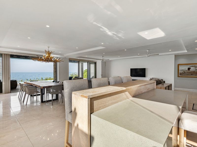 Spacious open-plan living and dining area featuring modern tiled floors, recessed lighting, and large sliding doors opening to a scenic ocean view.