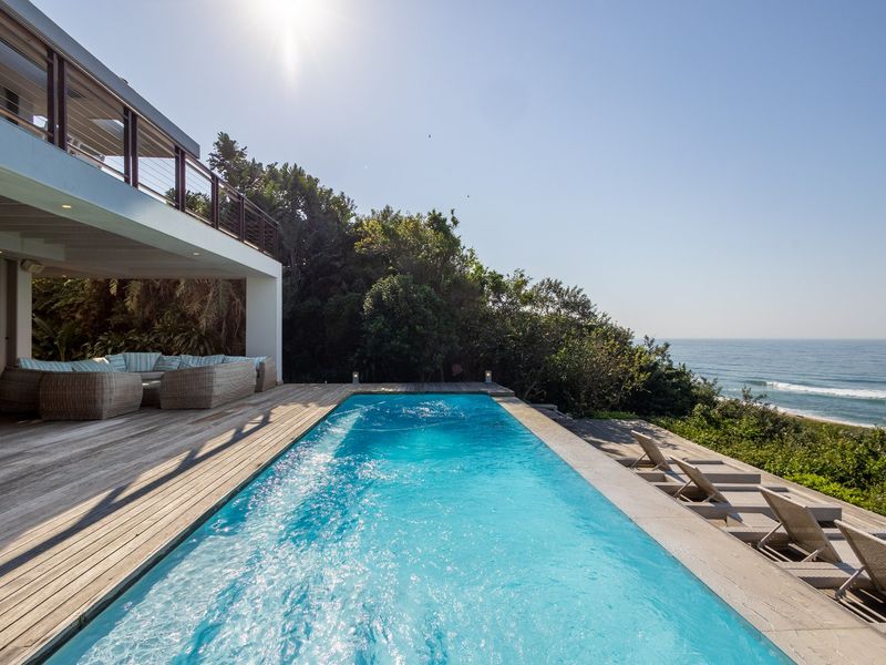 A stunning outdoor pool area featuring timber decking, a covered patio space, and direct ocean views.