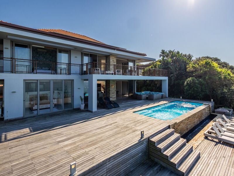 Rear view of a modern two-story home featuring a spacious timber deck, an integrated swimming pool, and a large upper-level balcony.