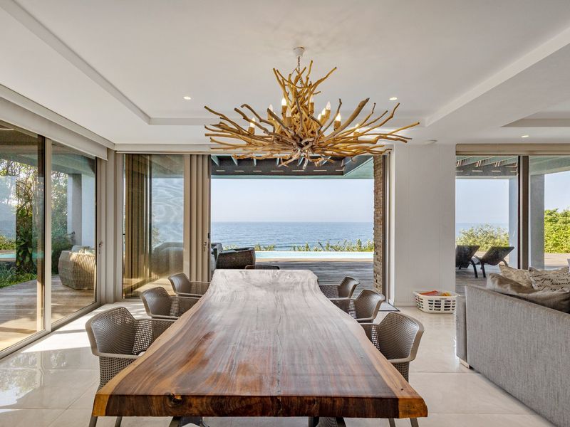 Spacious open-plan dining area featuring large sliding glass doors that open to a deck with ocean views and a modern tiled floor.