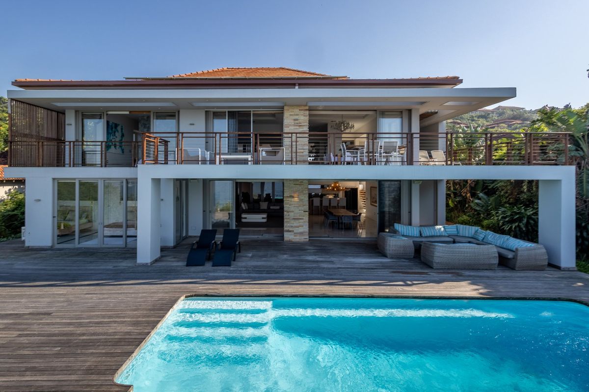 Rear elevation of a modern two-story residence featuring a swimming pool, expansive timber decking, and a spacious upper-level balcony with sliding glass doors.