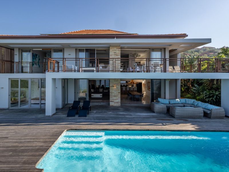 Rear elevation of a modern two-story residence featuring a swimming pool, expansive timber decking, and a spacious upper-level balcony with sliding glass doors.