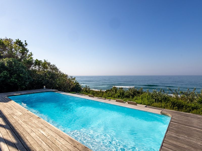 A stunning infinity-style swimming pool featuring timber decking, offering panoramic ocean views and a serene outdoor setting.